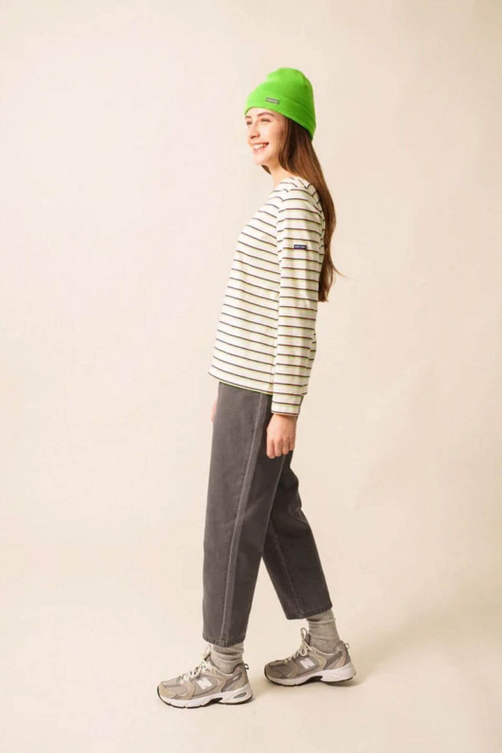 Woman wearing Chandail MINQUID.RAY TRI in vivid colors, green beanie, and grey pants for a vibrant winter look.