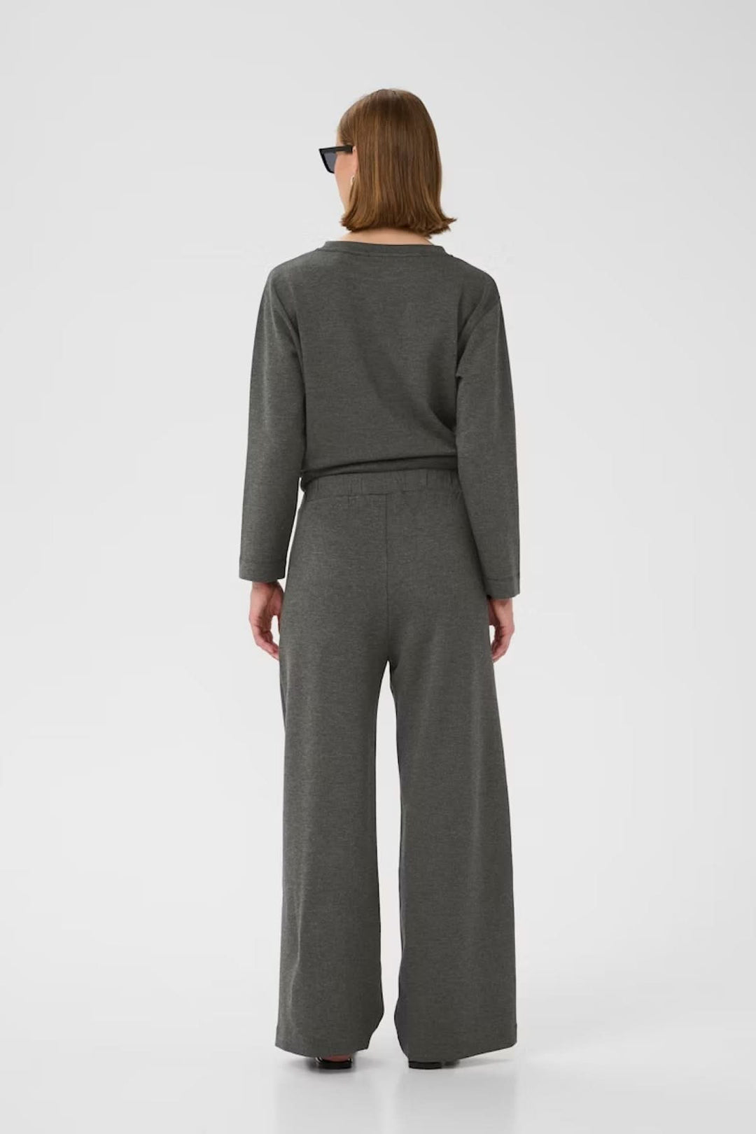 Femme vue de dos portant un pantalon large à taille haute gris, associé à un haut coordonné.