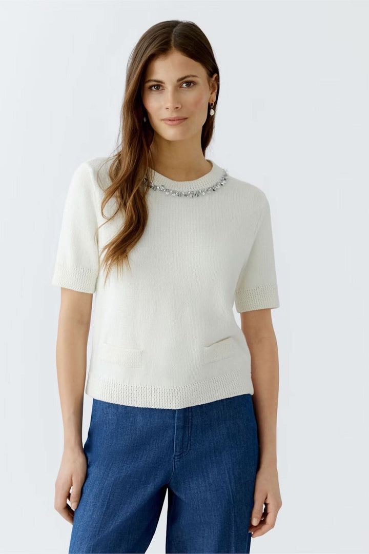 Chandail à col décoré en maille fine, manches courtes, avec perles et strass, porté avec un pantalon bleu.