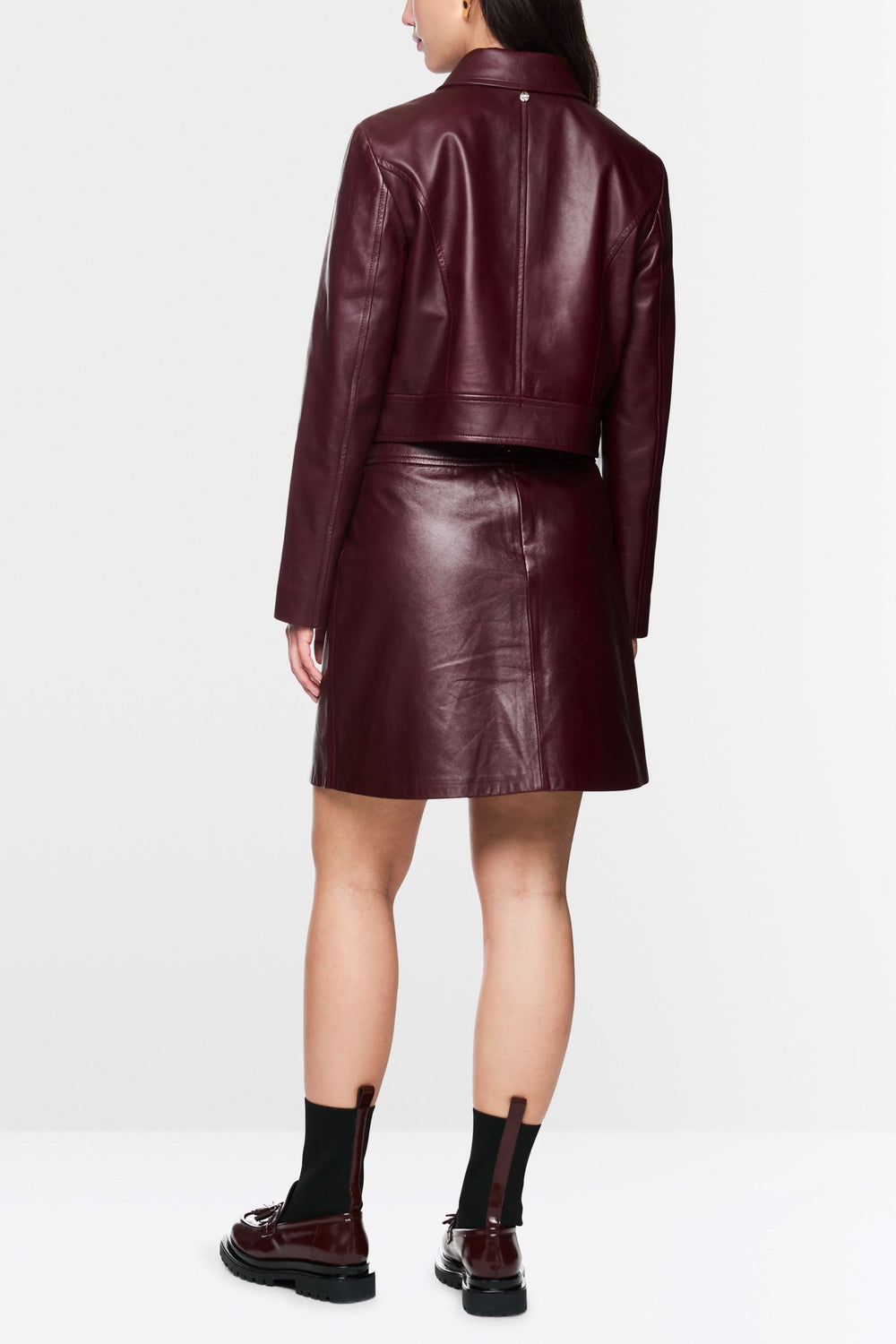 Veste en cuir bordeaux vue de dos, associée à une jupe en cuir, pour un look élégant et moderne.
