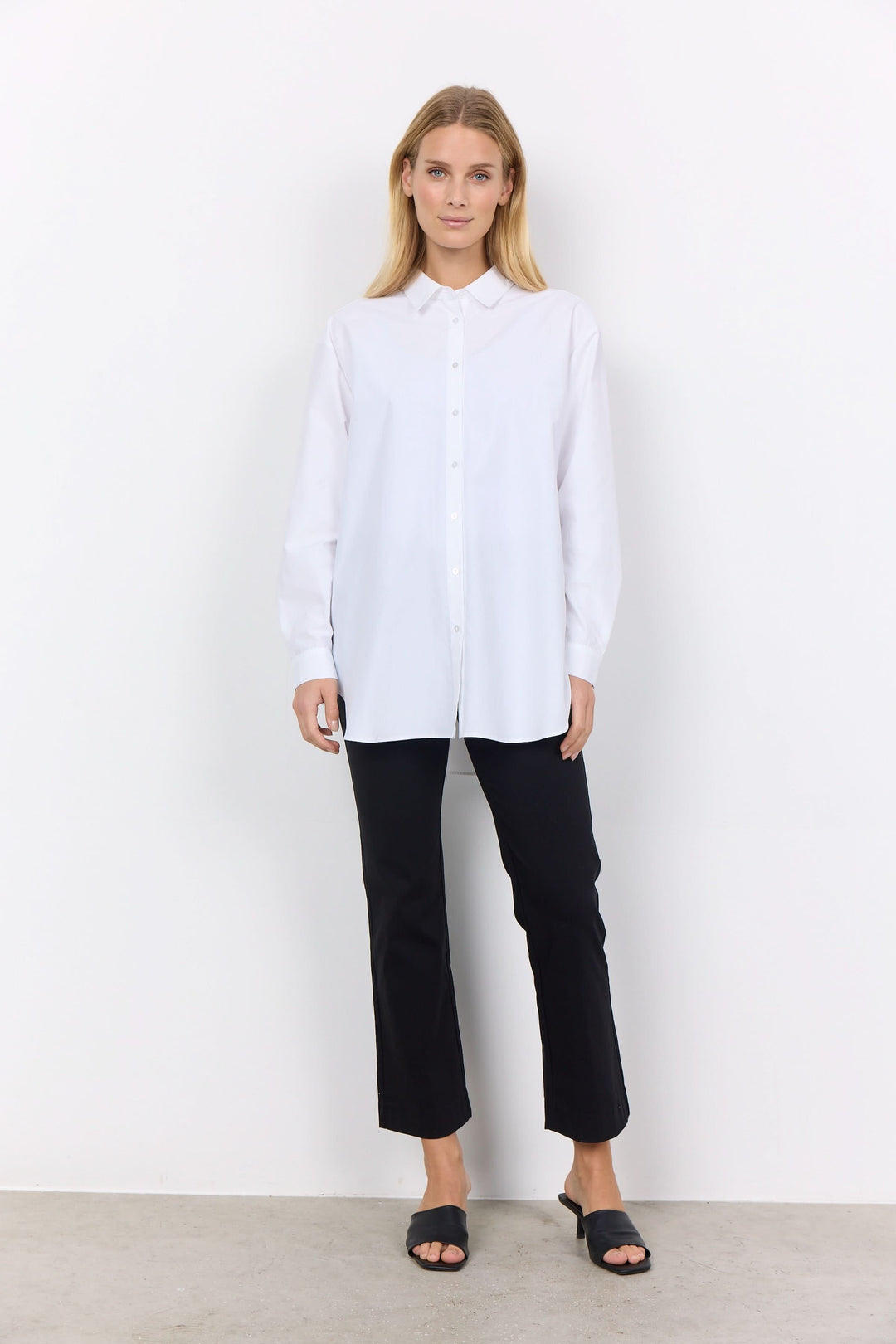 Chemise décontractée blanche à boutons, portée avec un pantalon noir moderne, pour une allure élégante et minimaliste.