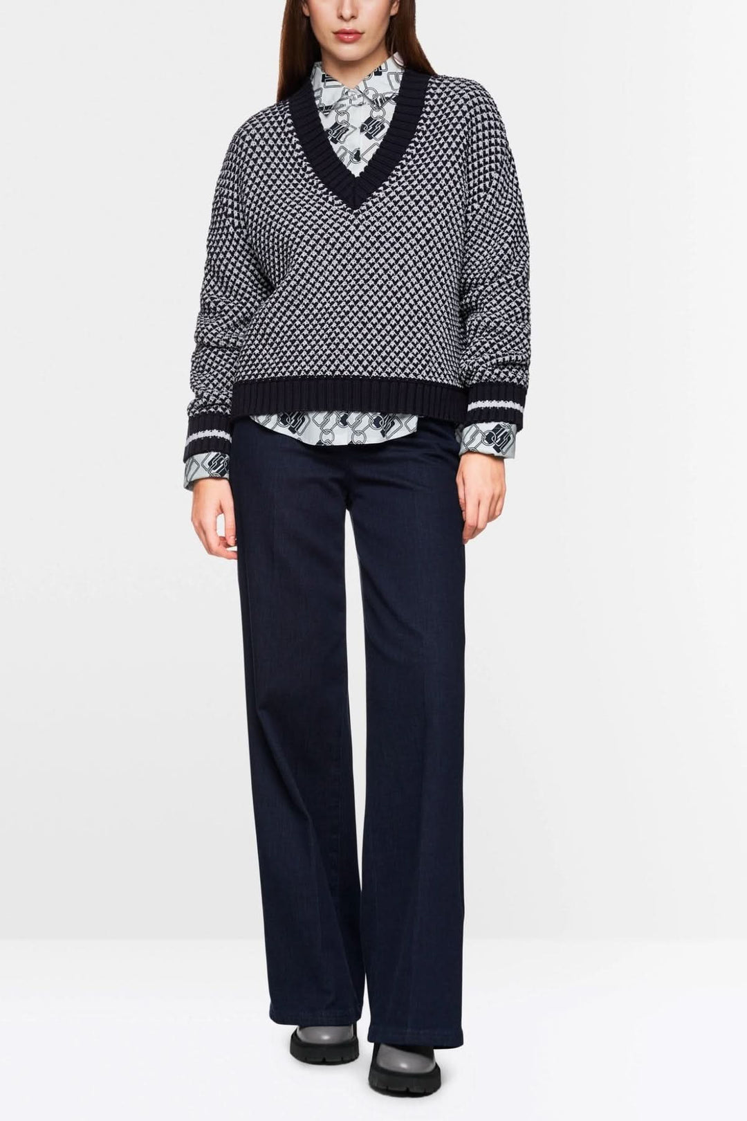 Pull court tricoté noir et blanc à encolure en V, porté avec une chemise à col et pantalon fluide.
