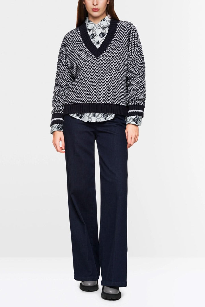 Pull court tricoté noir et blanc à encolure en V, porté avec une chemise à col et pantalon fluide.