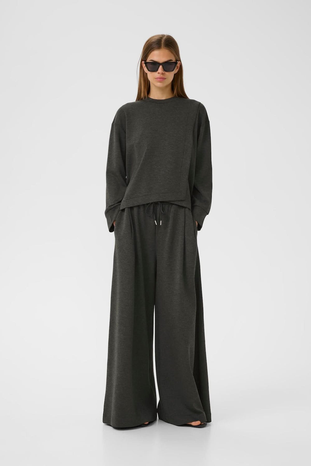 Chandail à emmanchures tombantes en gris, associé à un pantalon ample pour un look décontracté et contemporain.