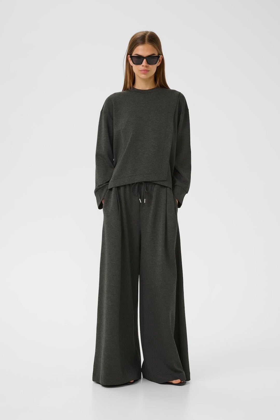 Chandail à emmanchures tombantes en gris, associé à un pantalon ample pour un look décontracté et contemporain.