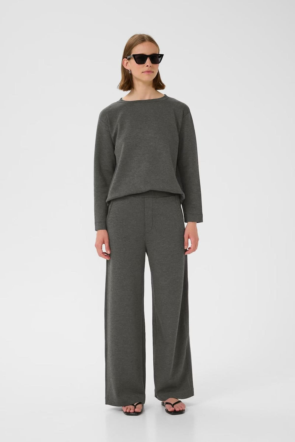 Femme portant un ensemble coordonné composé d'un pantalon large à taille haute et d'un chandail gris, avec lunettes de soleil.