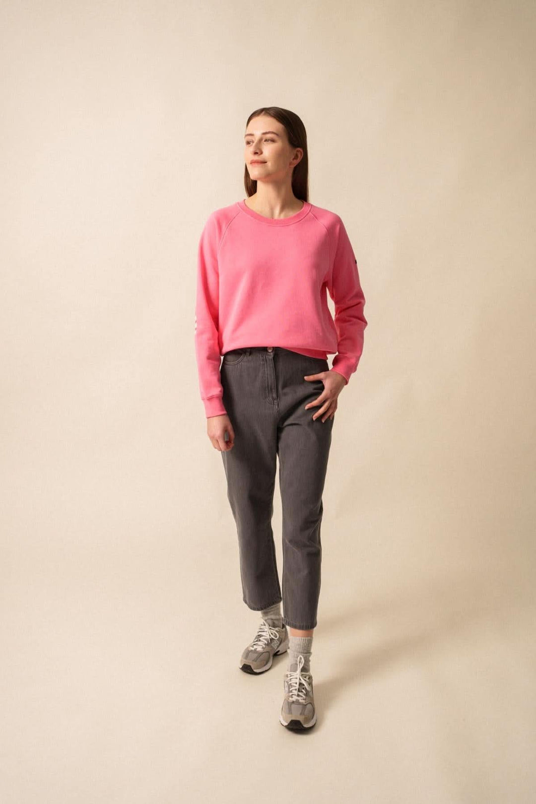 Femme portant un sweat rose, avec un pantalon gris, dans un style casual et confortable.