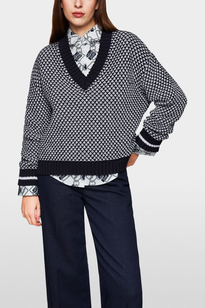 Pull court tricoté en noir et blanc avec encolure en V, porté sur une chemise à col noir et blanc.