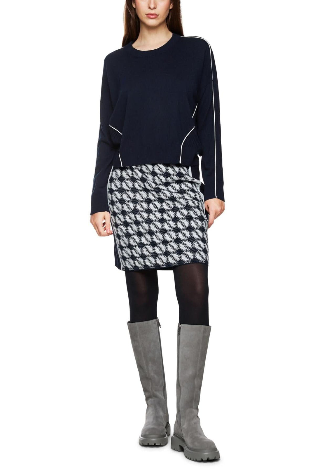 Femme en chandail en laine et cachemire, jupe à motif, collants noirs et bottes grises.