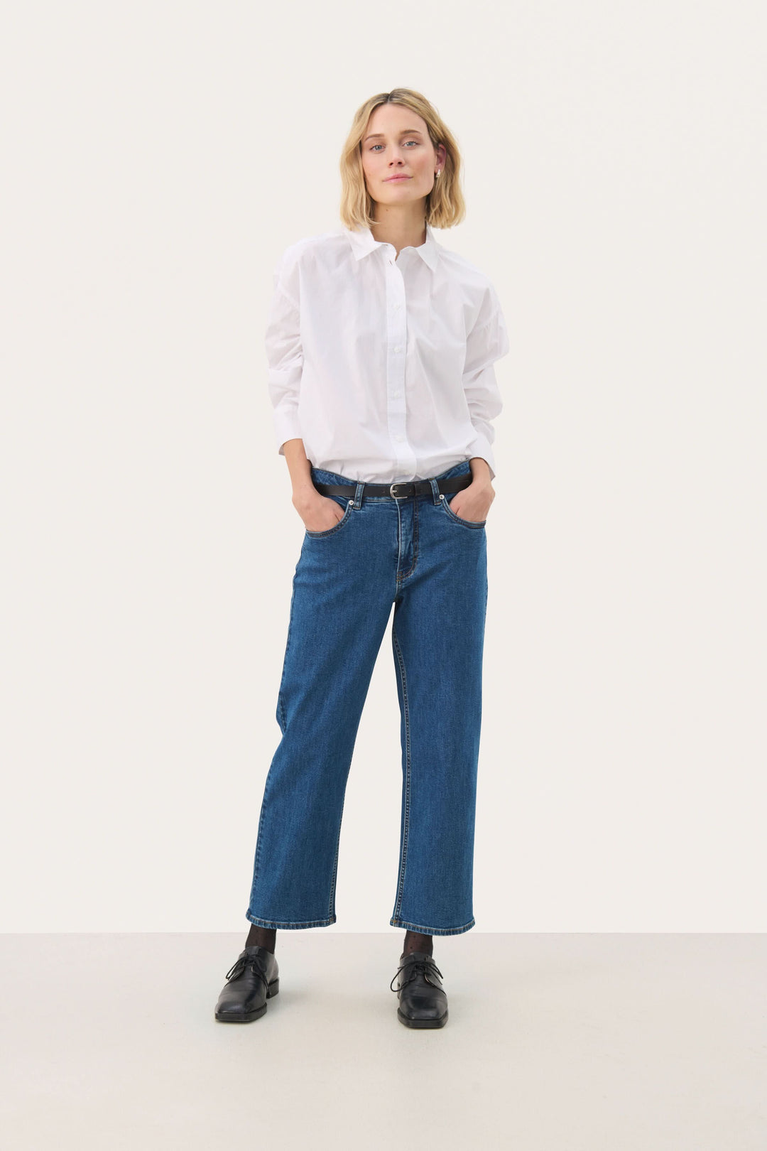 Femme portant un jean à jambe droite écourtée avec une chemise blanche, créant un look décontracté et moderne.