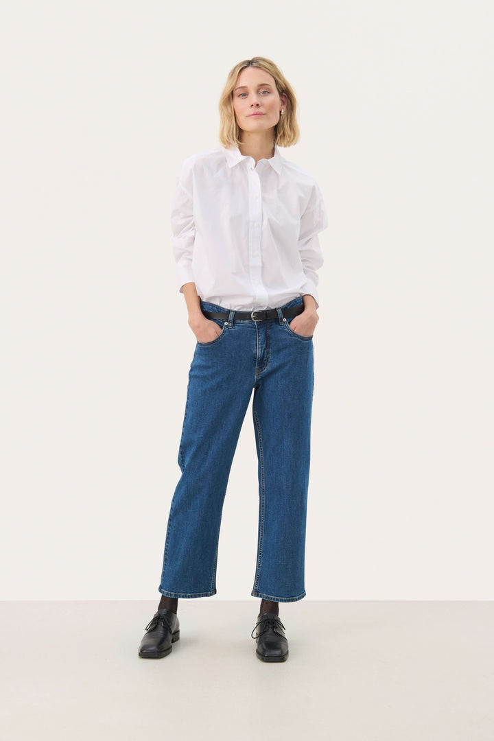 Femme portant un jean à jambe droite écourtée avec une chemise blanche, créant un look décontracté et moderne.