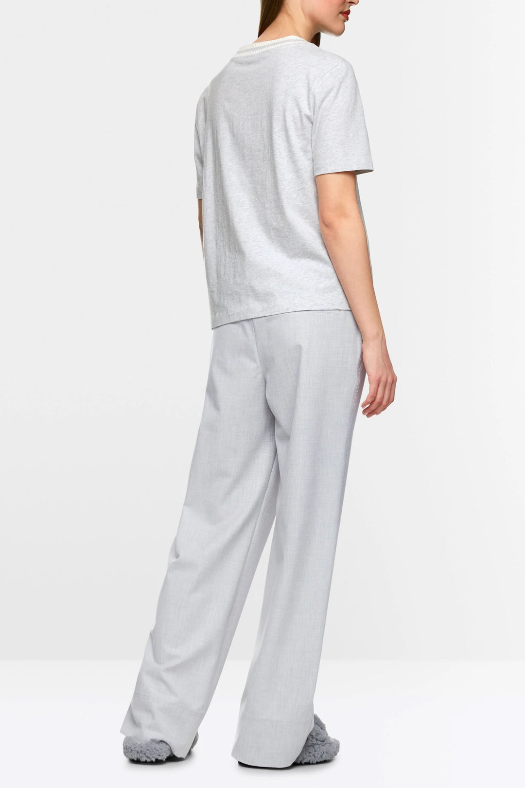 Femme portant un t-shirt gris sobre et un pantalon gris large, vue de dos, dans un style décontracté et moderne.