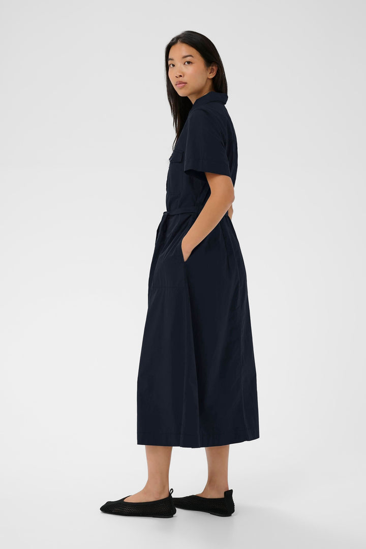 Femme portant la Robe Ariel chemise longue ceinturée manches courtes, élégante et structurée, avec ceinture et manches courtes.