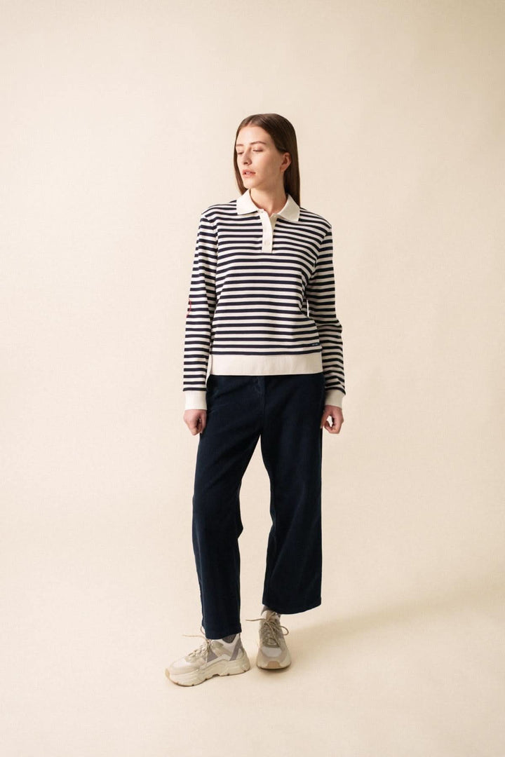 Chandail polo NINA à rayures avec col classique, porté avec un pantalon noir pour un look décontracté.