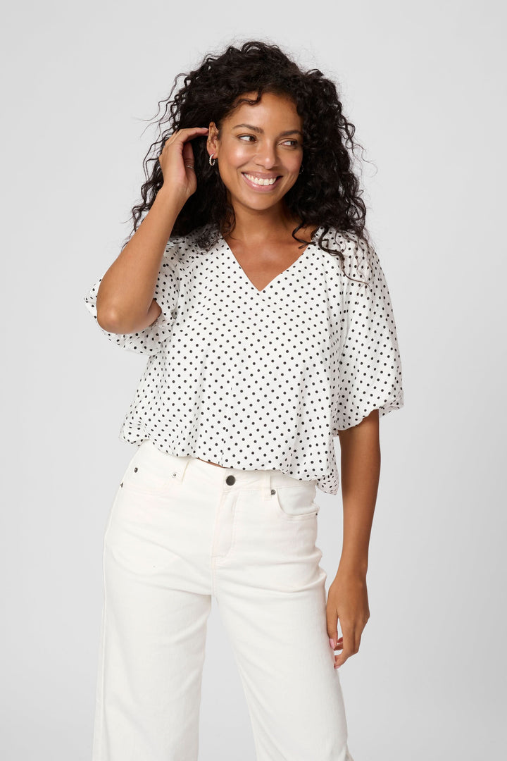 Blouse Gwen à pois avec encolure en V, manches amples, look aérien et moderne, portée avec un jean taille haute.