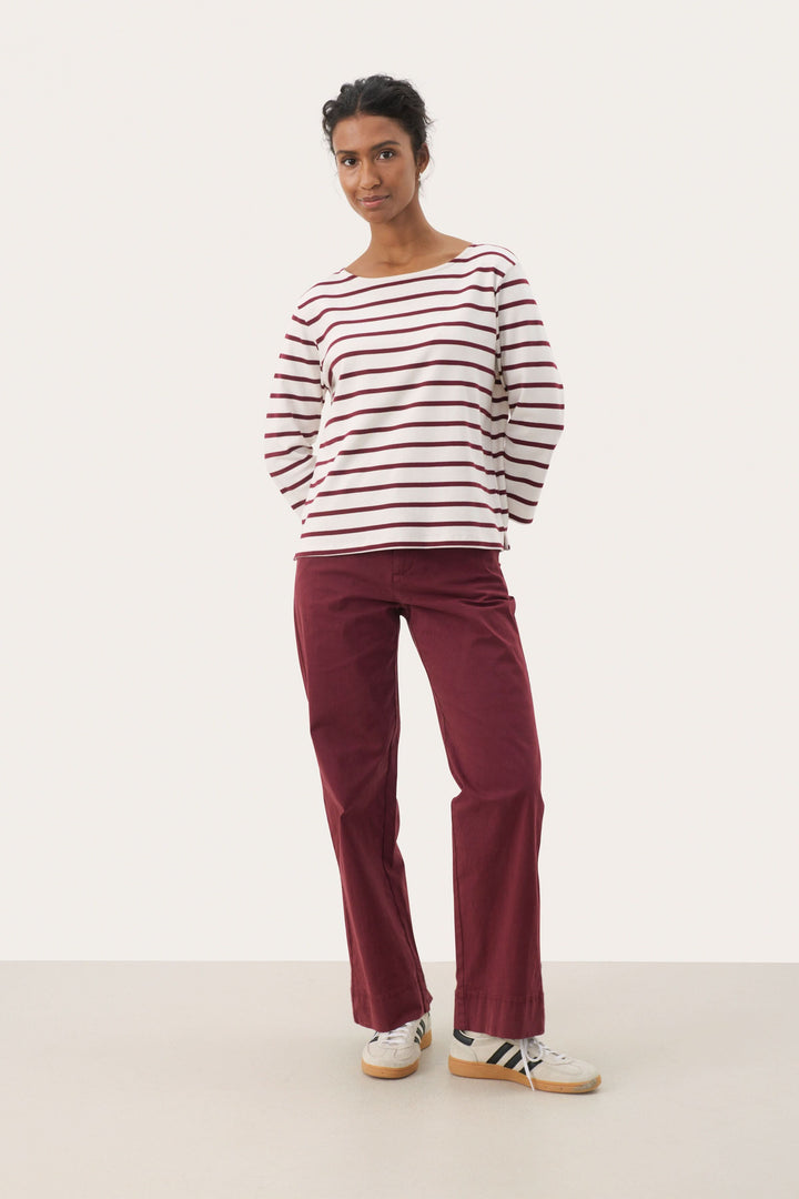 Chandail Nela rayé à manches longues, col bateau, associé à un pantalon bordeaux pour un look casual chic.