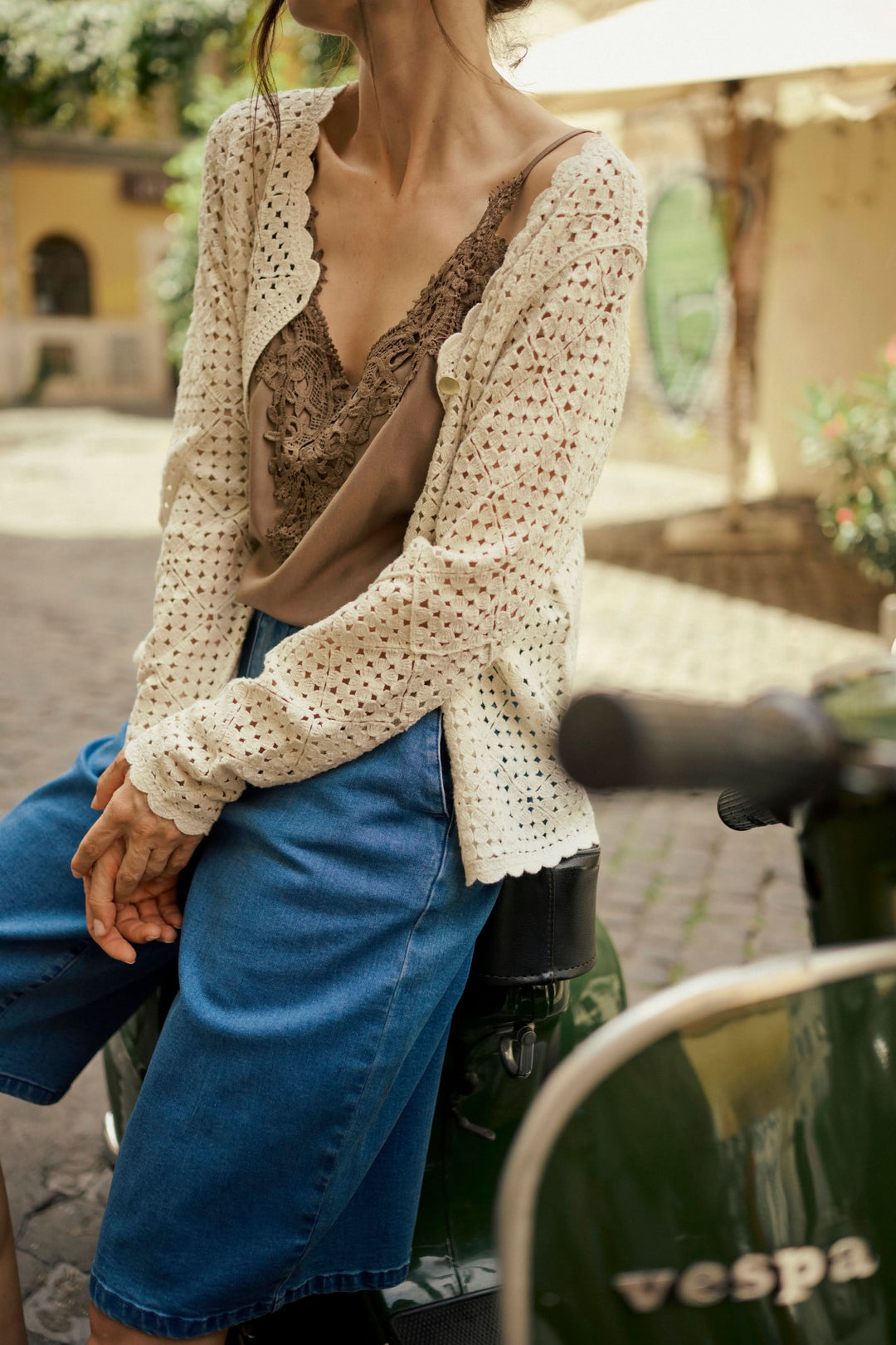 Cardigan ajouré beige sur une femme, combiné avec un haut marron et un short en jean, devant une vespa.