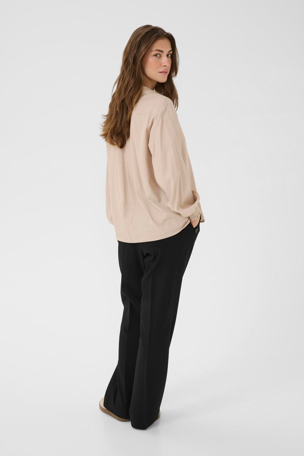 Woman wearing the Blouse Nola fluide à poignets smockés with casual pants, viewed from the side.