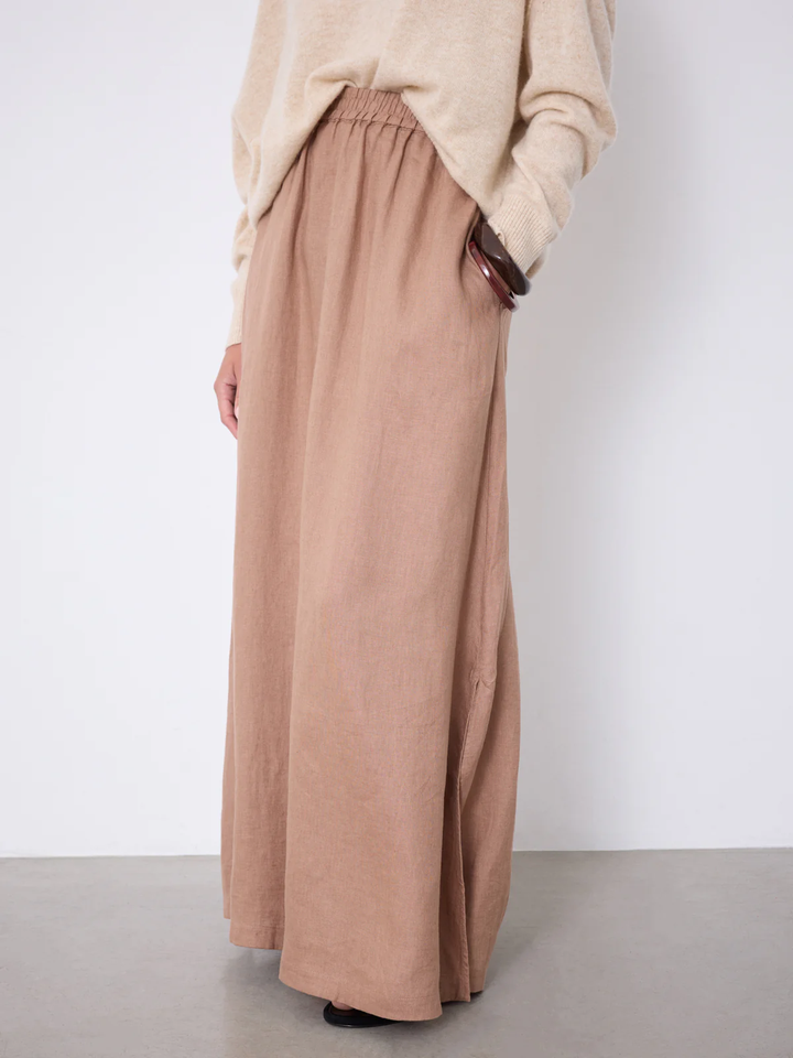 Femme portant une Jupe Vivienne longue fluide taille élastique beige avec poches et fente latérale, style élégant et estival.