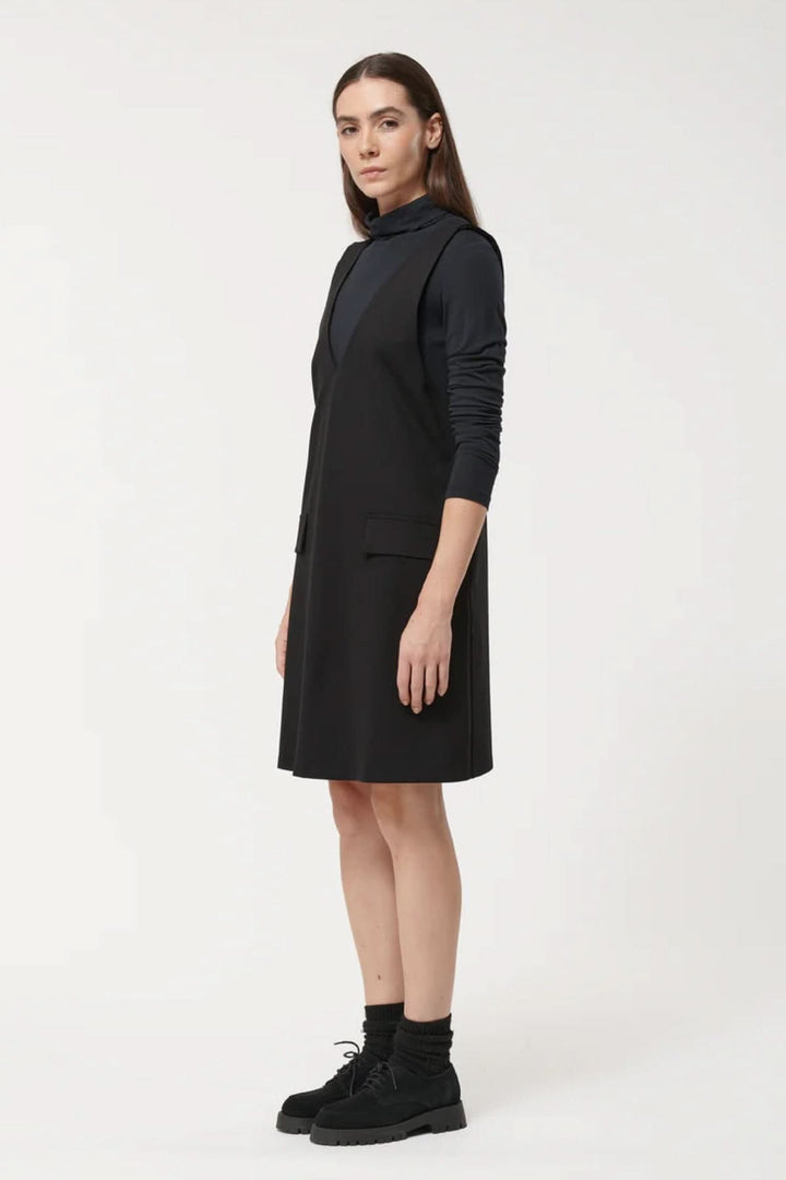 Robe sans manches chic à encolure en V et coupe évasée, portée avec un sous-pull noir pour un look minimaliste et polyvalent.
