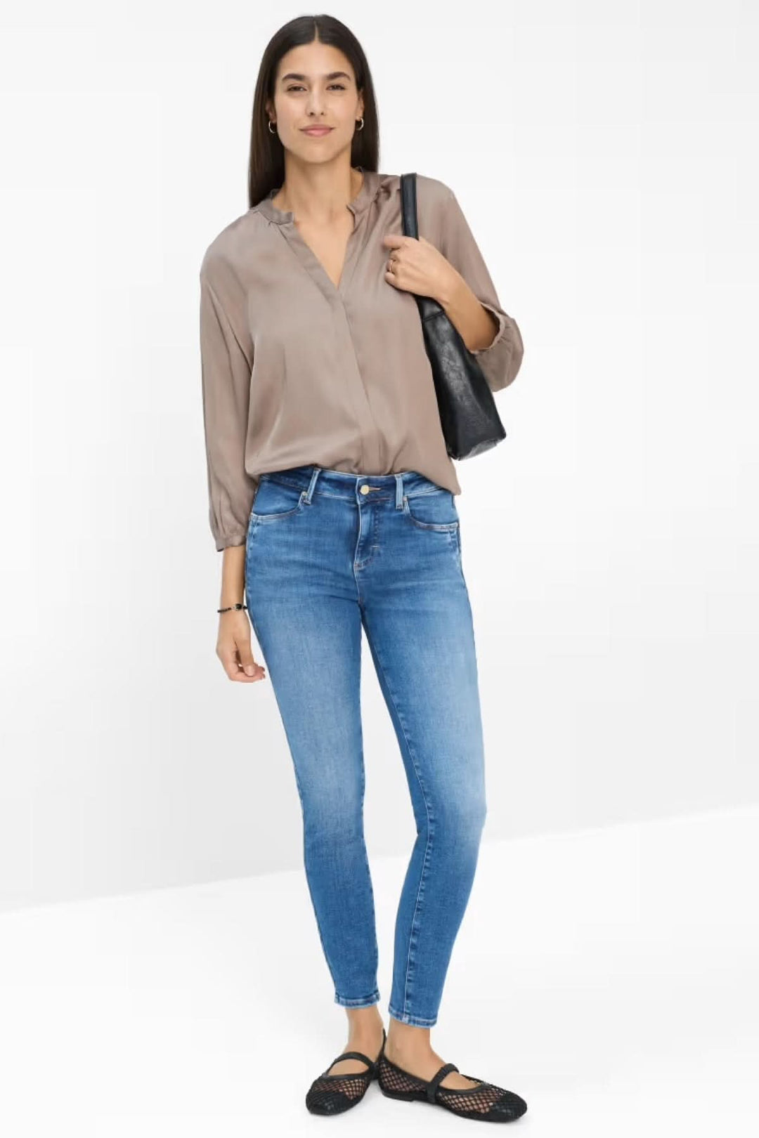 Femme en blouse fluide et jean skinny bleu clair, look chic et décontracté, sac noir en bandoulière.