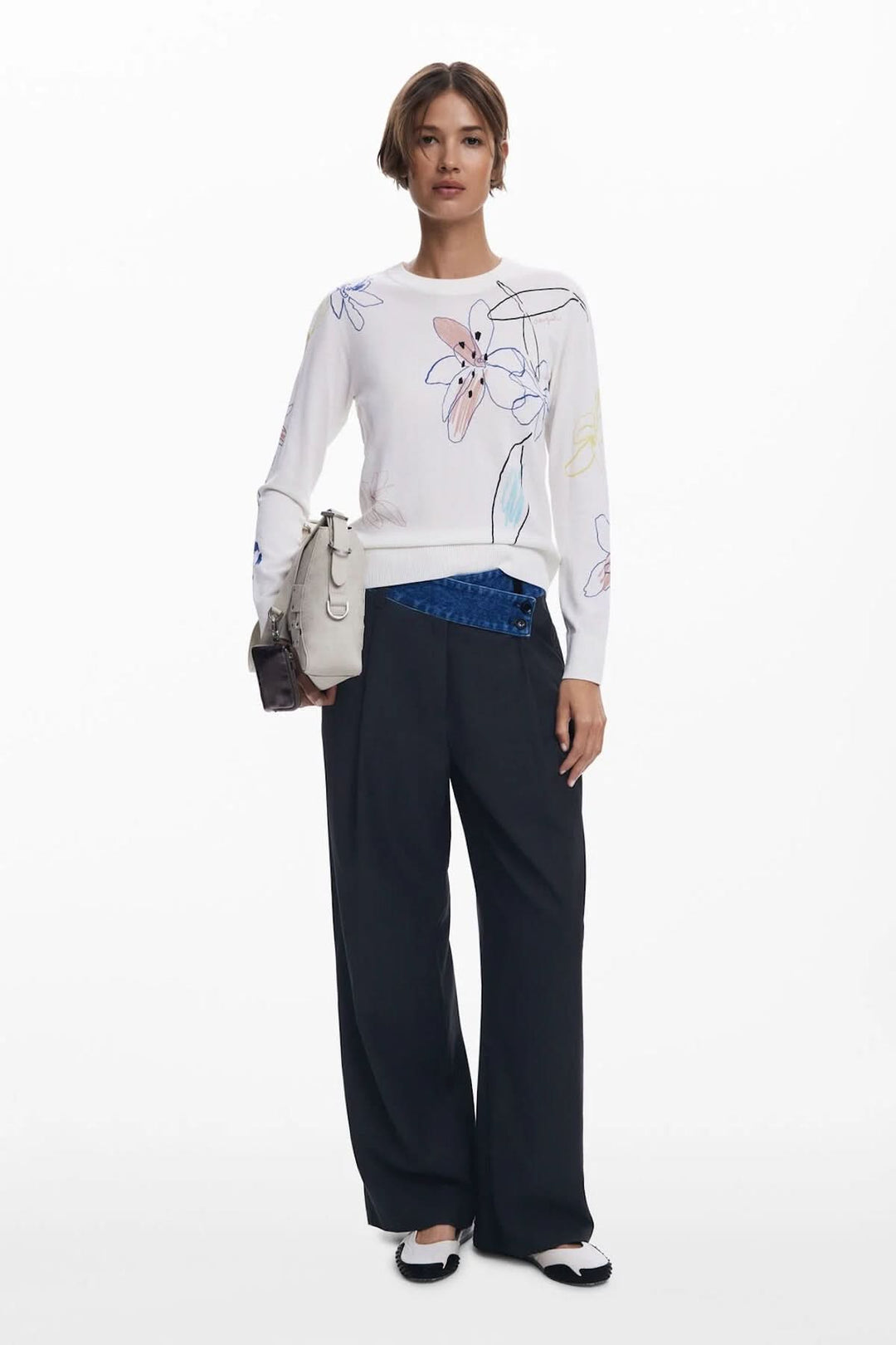Femme portant un chandail léger à motif floral avec un pantalon noir et un élégant sac à main.