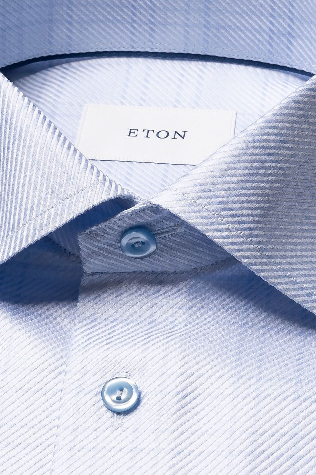 Chemise en coton bleu clair à carreaux fins avec col ouvert et boutons, offrant une élégance moderne et un confort texturé.