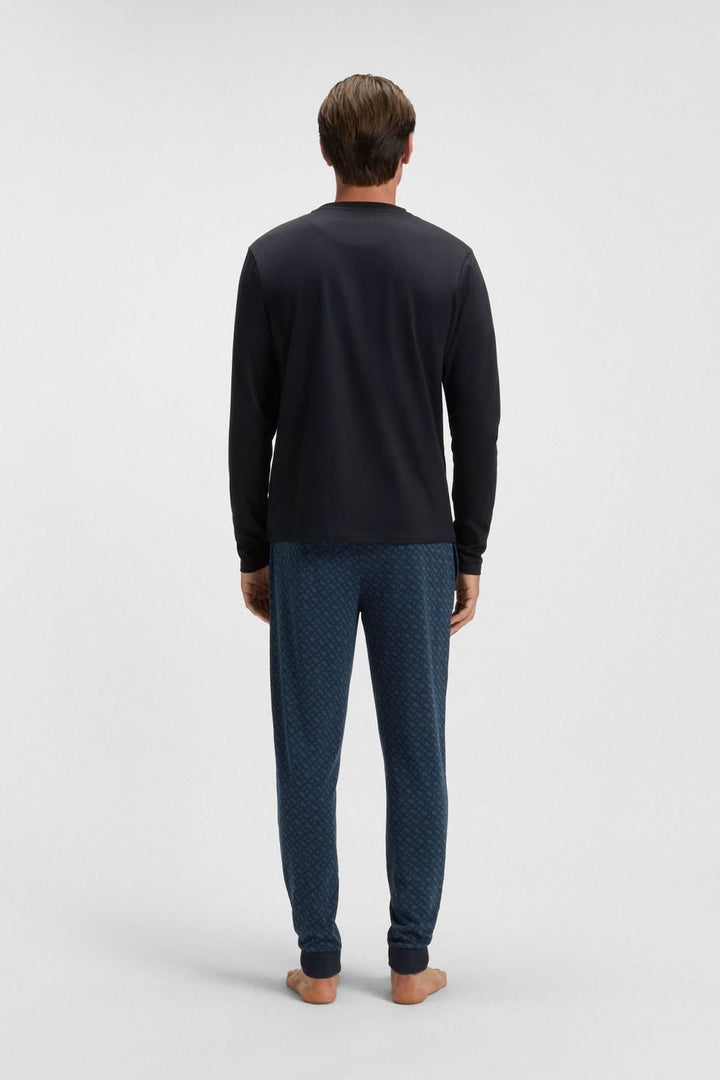 Homme portant un ensemble pyjama en coton avec logo BOSS, vu de dos, composé d'un haut noir et d'un pantalon bleu à motifs.