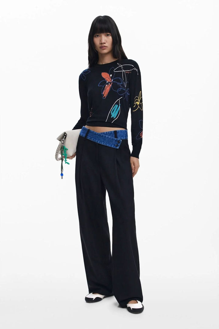 Modèle portant un chandail léger floral à col rond et un pantalon large, avec une sacoche élégante.