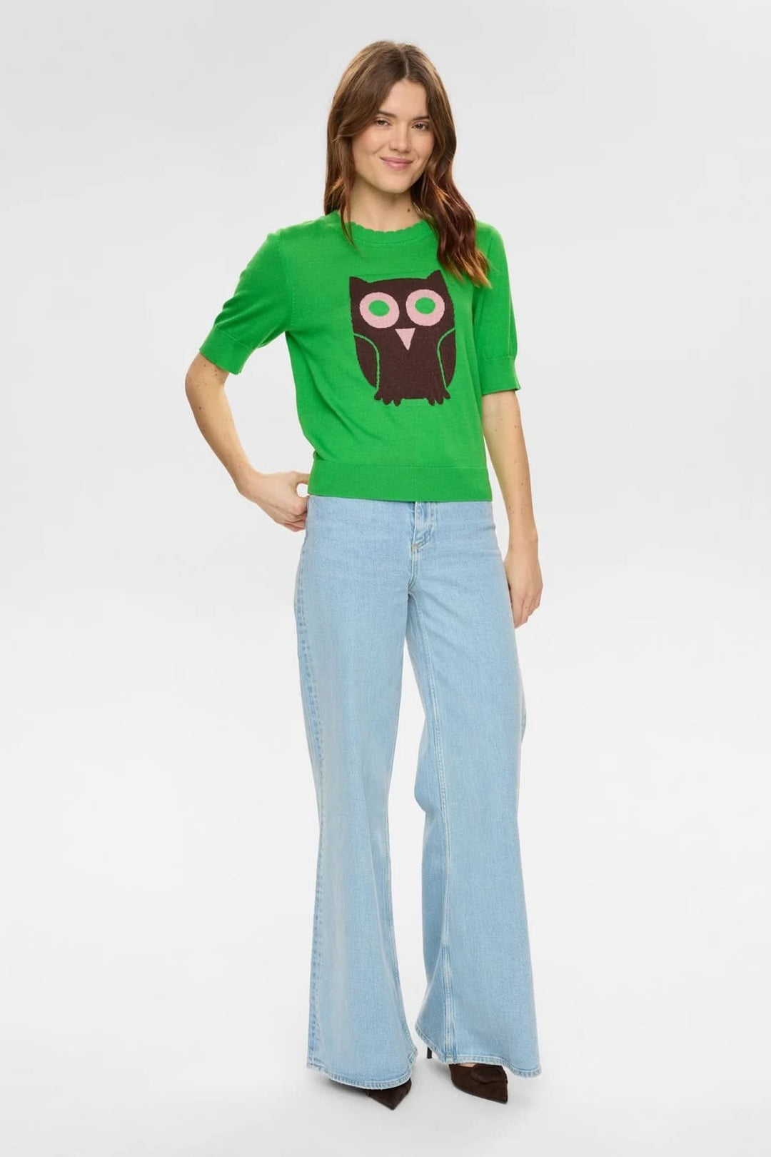 Femme portant un chandail en tricot motif hibou vert avec jean évasé, style moderne et ludique. Décris moi le produit en français.