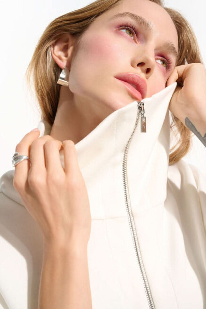 Femme portant une veste zippée à col large en blanc, illustrant l'élégance moderne et confortable du vêtement. Décris moi le produit.