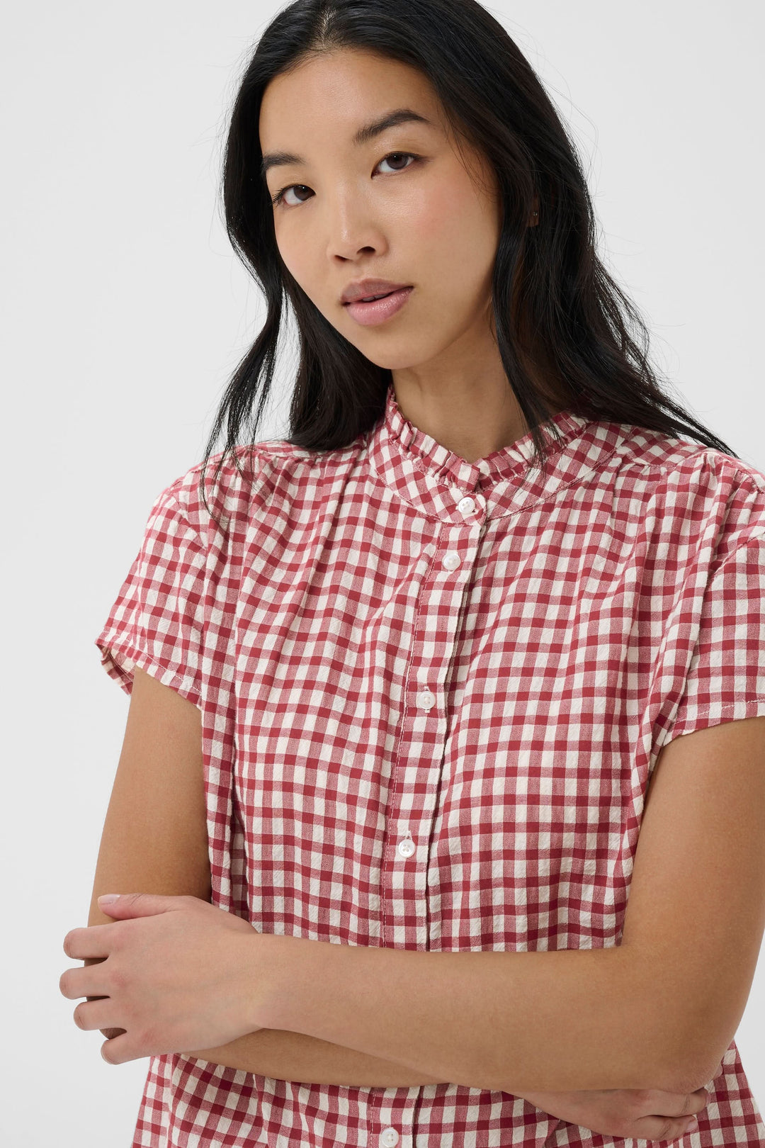 Blouse Bjanka à carreaux col montant boutonné portée par une femme, manches courtes et motif à carreaux rouge et blanc.