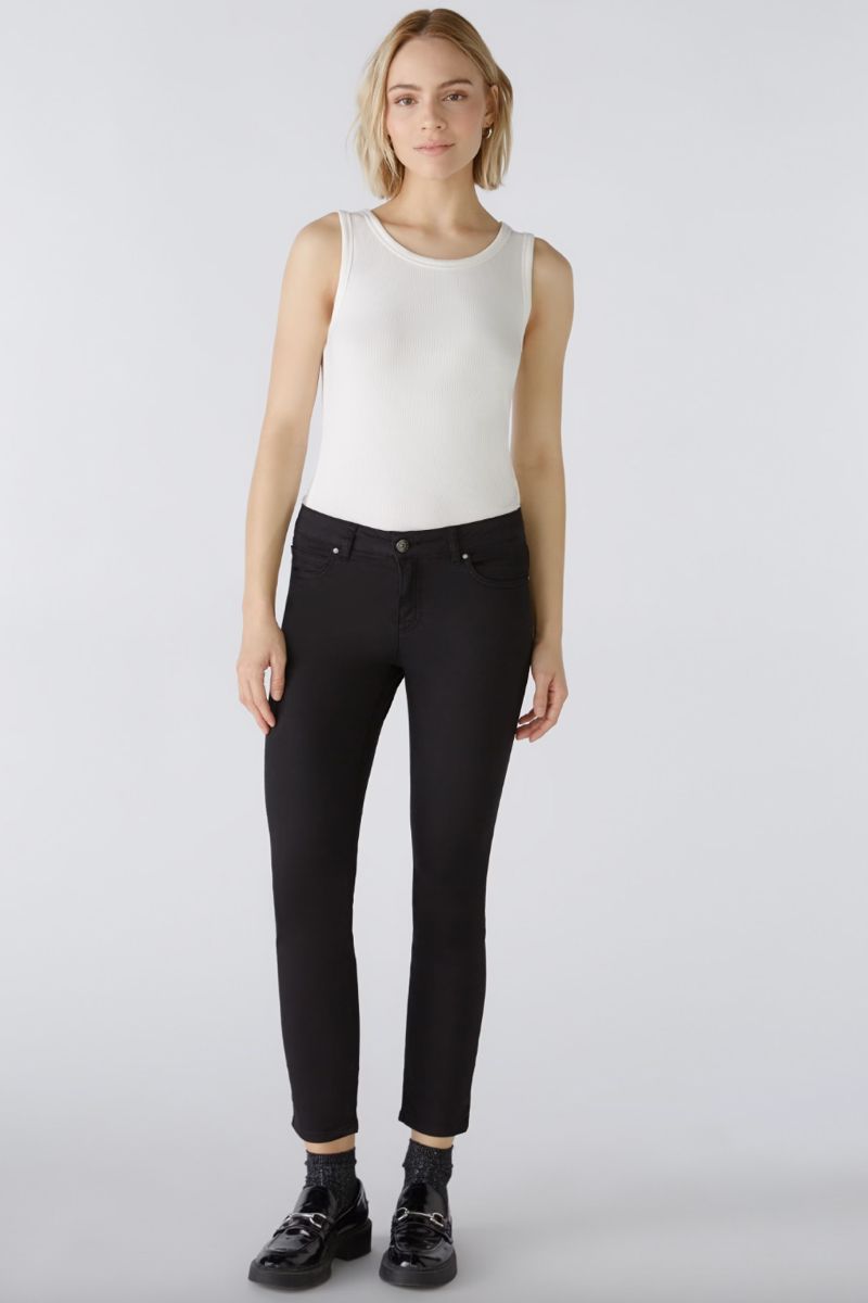 Femme portant un pantalon ajusté noir, coupe moderne, avec un débardeur blanc, style décontracté.
