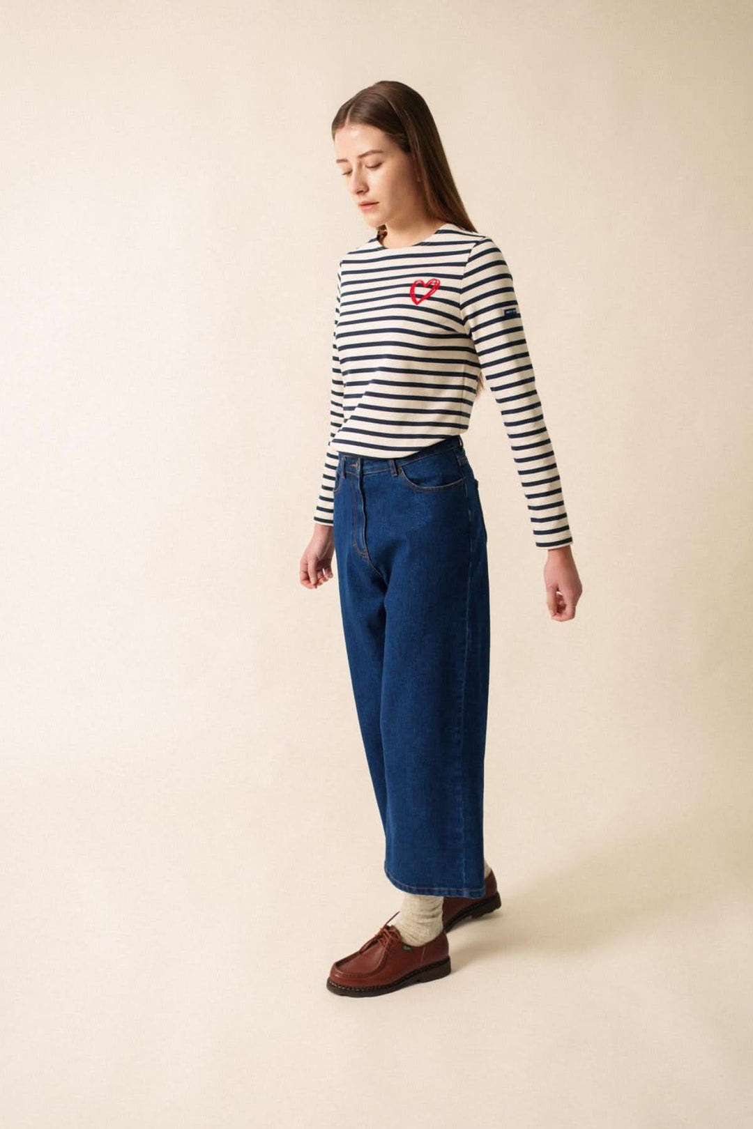 Femme en chandail rayé avec motif cœur, portant un jean bleu pour un look casual-chic.
