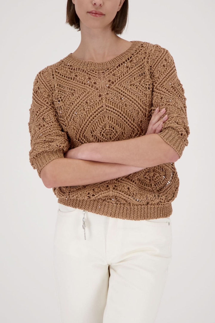 Femme portant un tricot ajouré à motifs beige avec détails travaillés, idéal pour un style moderne et raffiné.