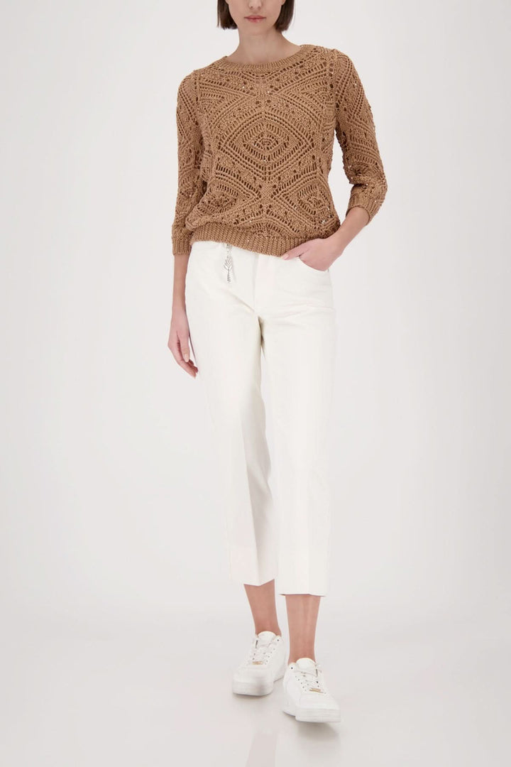 Tricot ajouré à motifs marron avec manches trois-quarts, porté sur un pantalon blanc, créant un look moderne et raffiné.