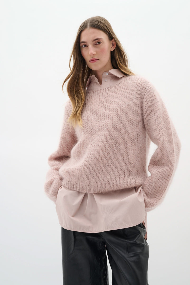 Chandail Jetra en maille duveteuse rose, porté sur un chemisier, avec un look élégant et cosy.