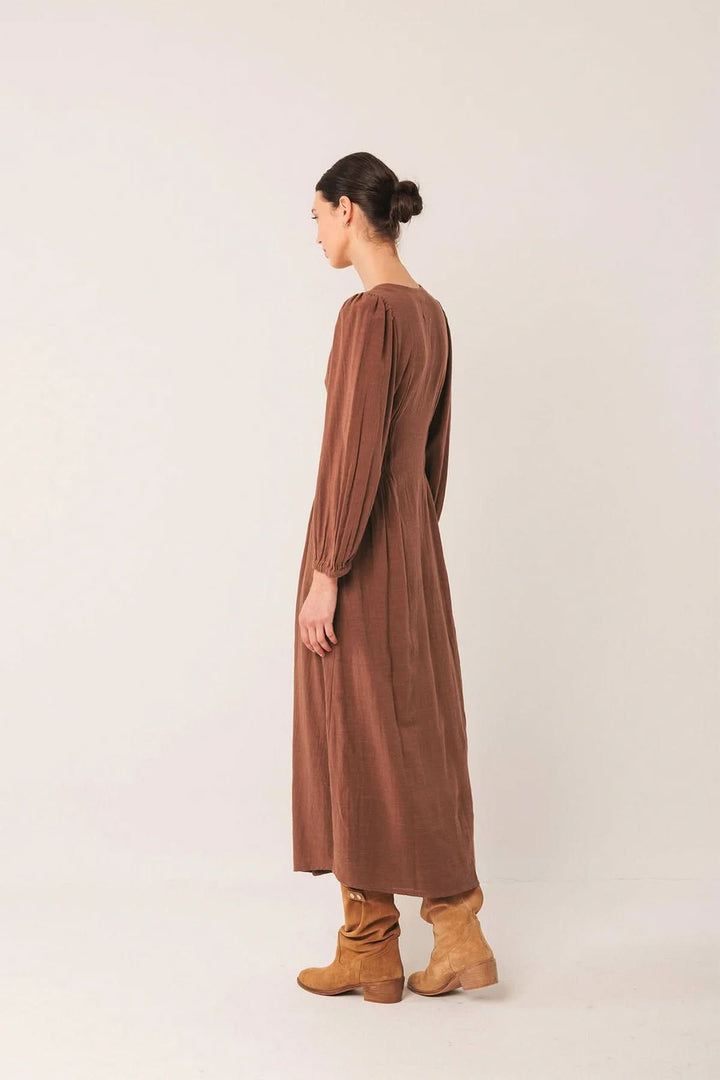Femme portant une robe longue à encolure V et manches bouffantes, vue de côté, style moderne avec bottes marron, robe fluide.