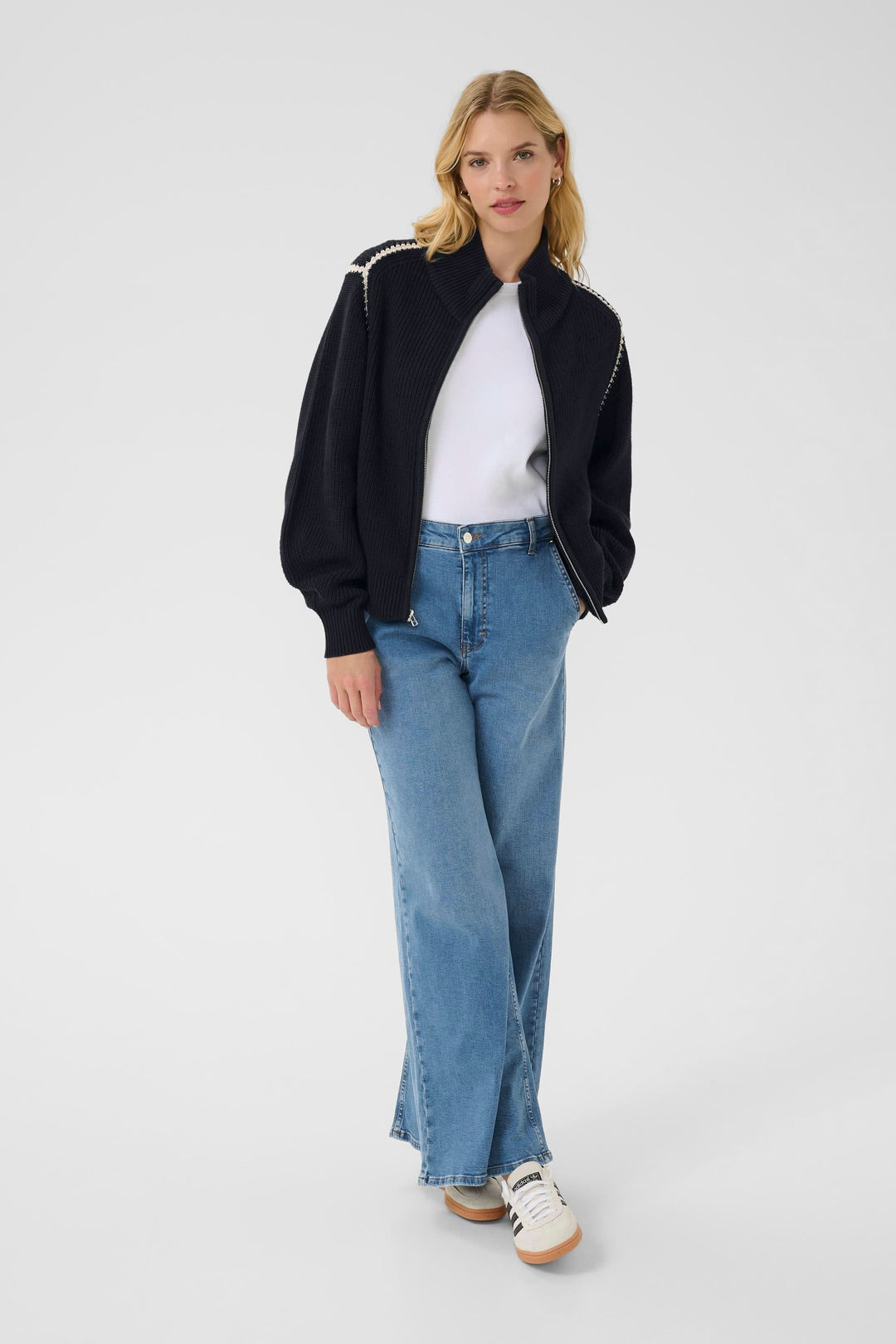 Femme portant une veste zippée Semra en maille noir, t-shirt blanc et jean large, look casual moderne.