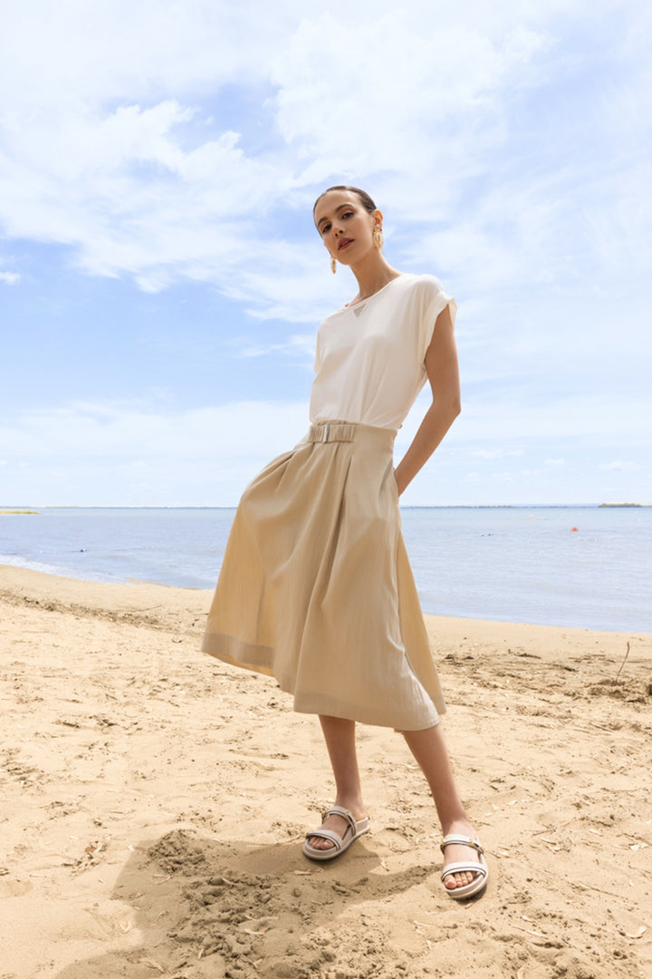 Femme portant une robe midi fluide à taille ceinturée sur la plage, combinant élégance décontractée avec confort quotidien.