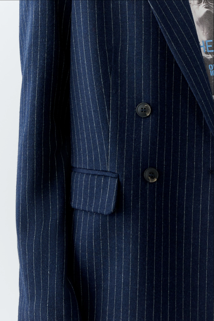 Détail d'un veston en jersey doux, rayures bleu marine et blanches, design moderne à double boutonnage.