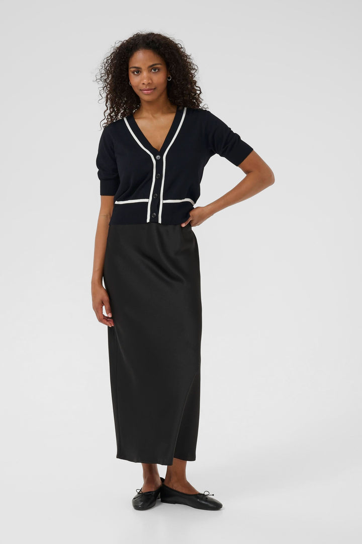 Femme portant un cardigan Lizza court à manches courtes, avec jupe noire, style chic et élégant.