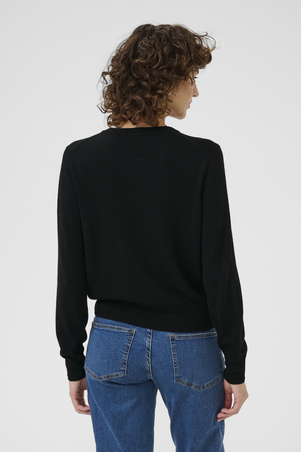 Femme vue de dos portant un cardigan noir en laine douce, associé à un jean bleu décontracté.