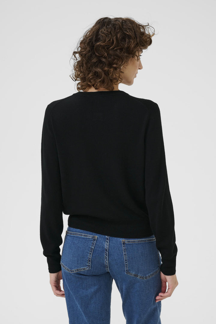 Femme vue de dos portant un cardigan noir en laine douce, associé à un jean bleu décontracté.