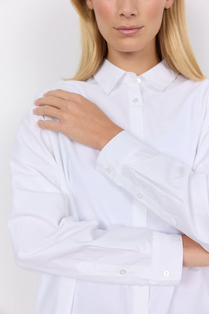 Chemise décontractée blanche à col classique, offrant élégance et confort, portée par une femme.