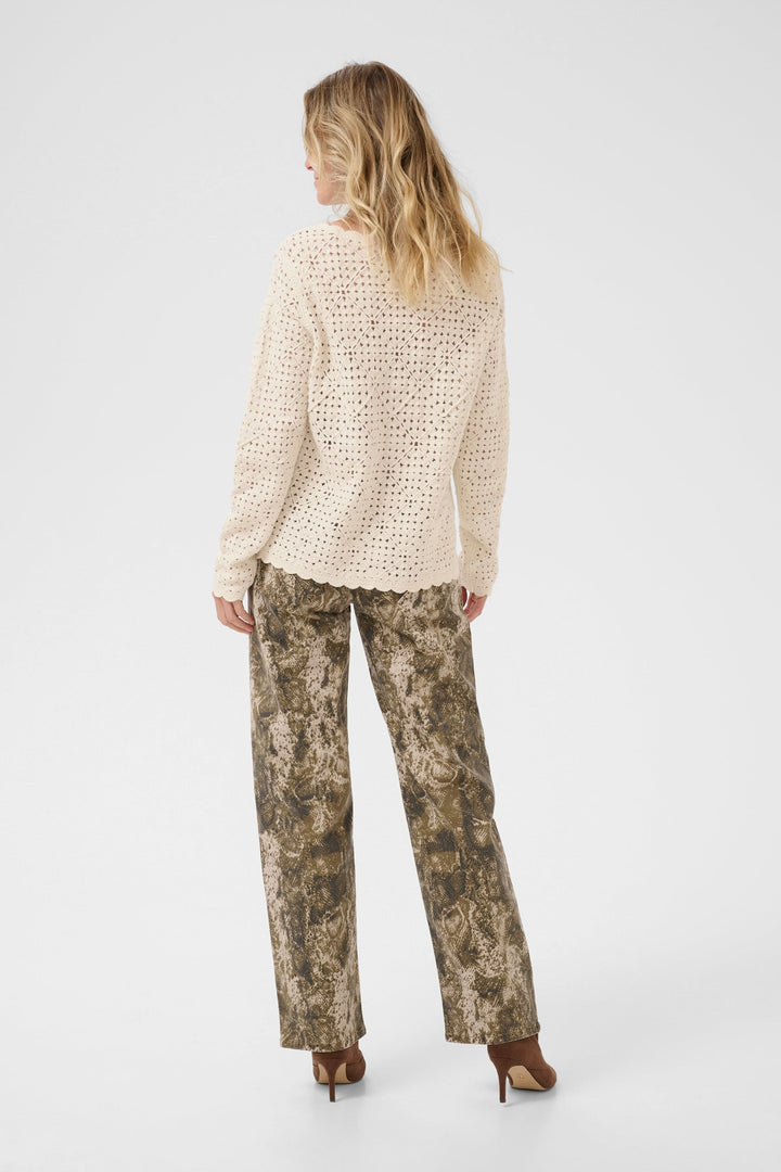Femme de dos portant un cardigan ajouré crème avec un pantalon imprimé terre, style élégant et contemporain.