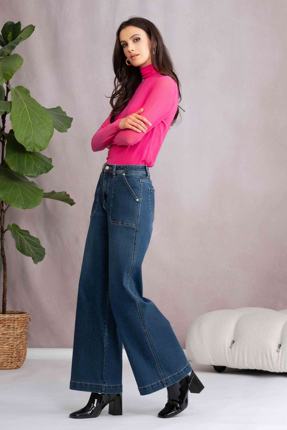 Femme portant un jean jambe évasée à taille haute avec un haut ajusté rose, dans un décor moderne.