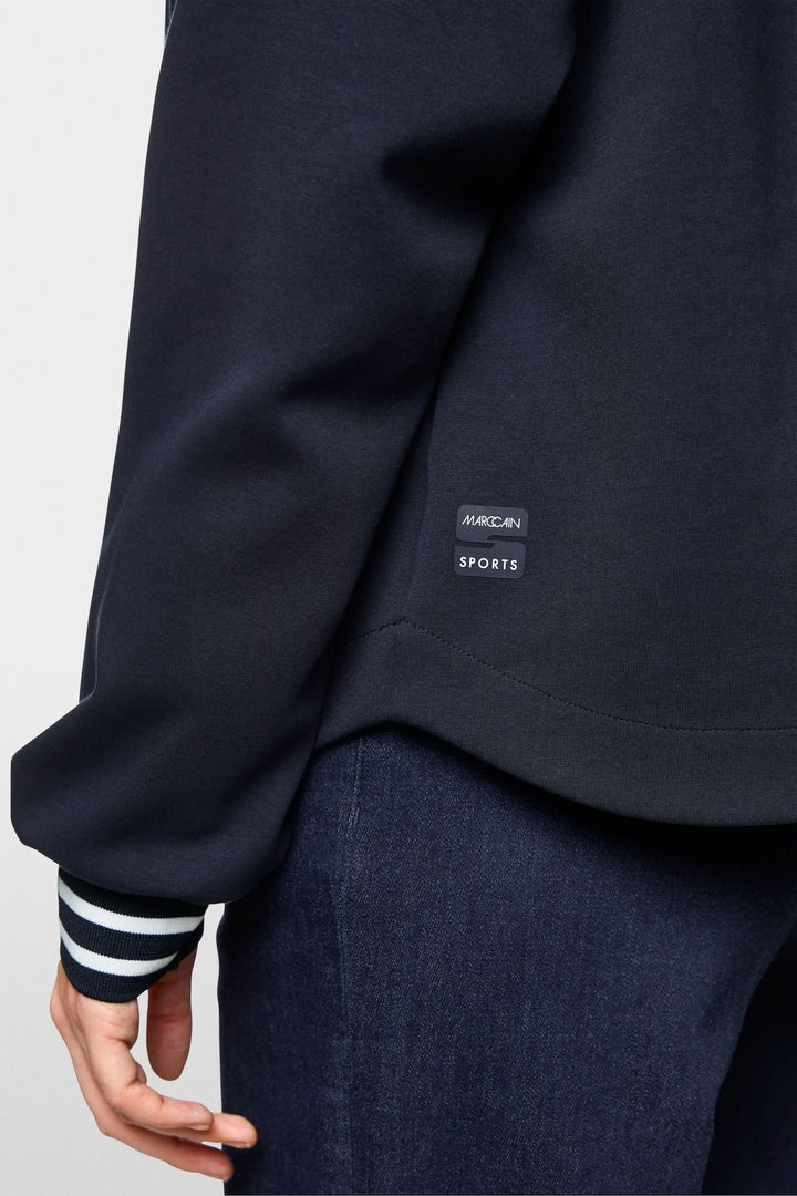 Détail d'un sweat-shirt à fermeture éclair avec étiquette sportive, coupe ample et manches rayées.
