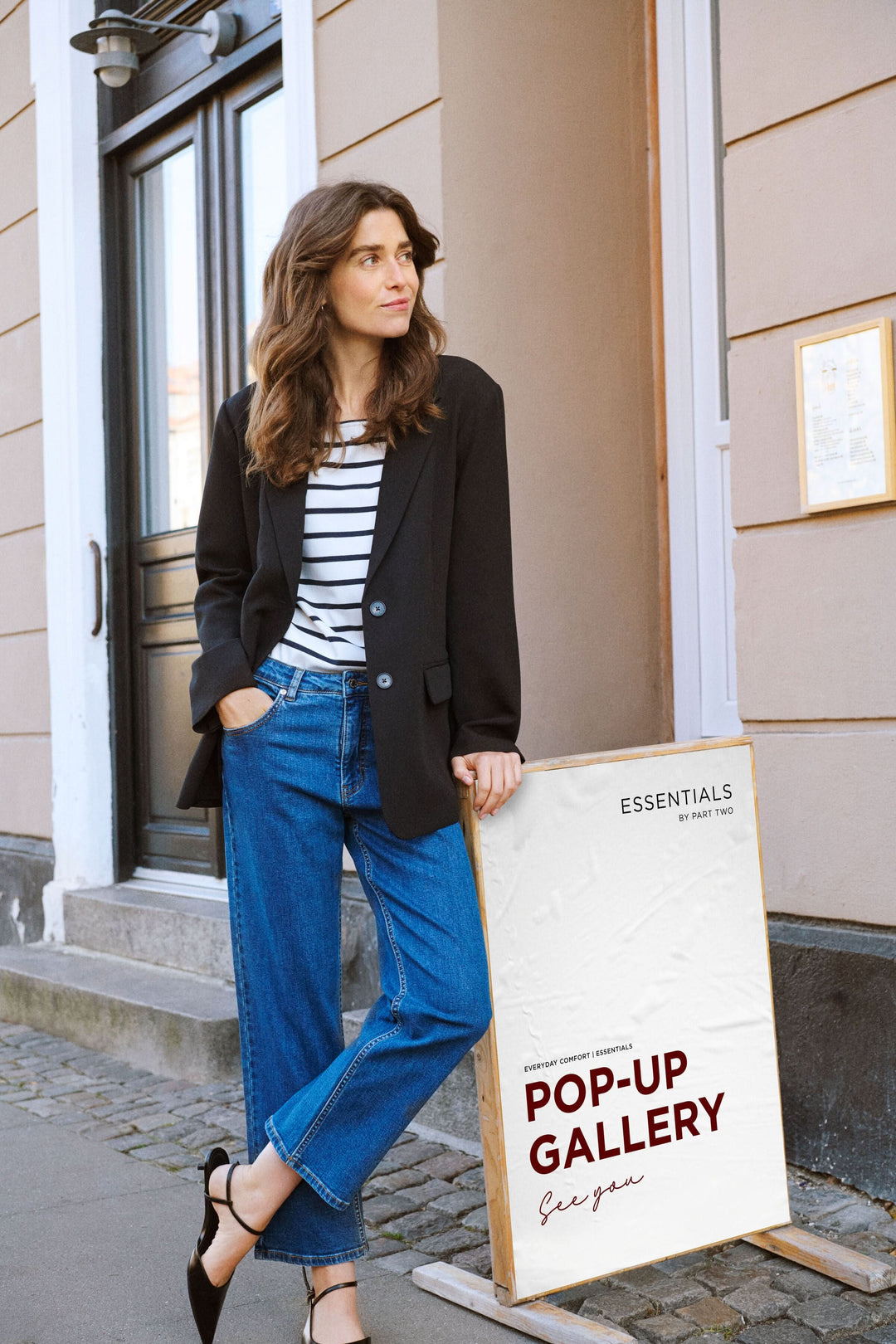 Femme en blazer noir et jean décontracté devant une galerie, style moderne et chic.
