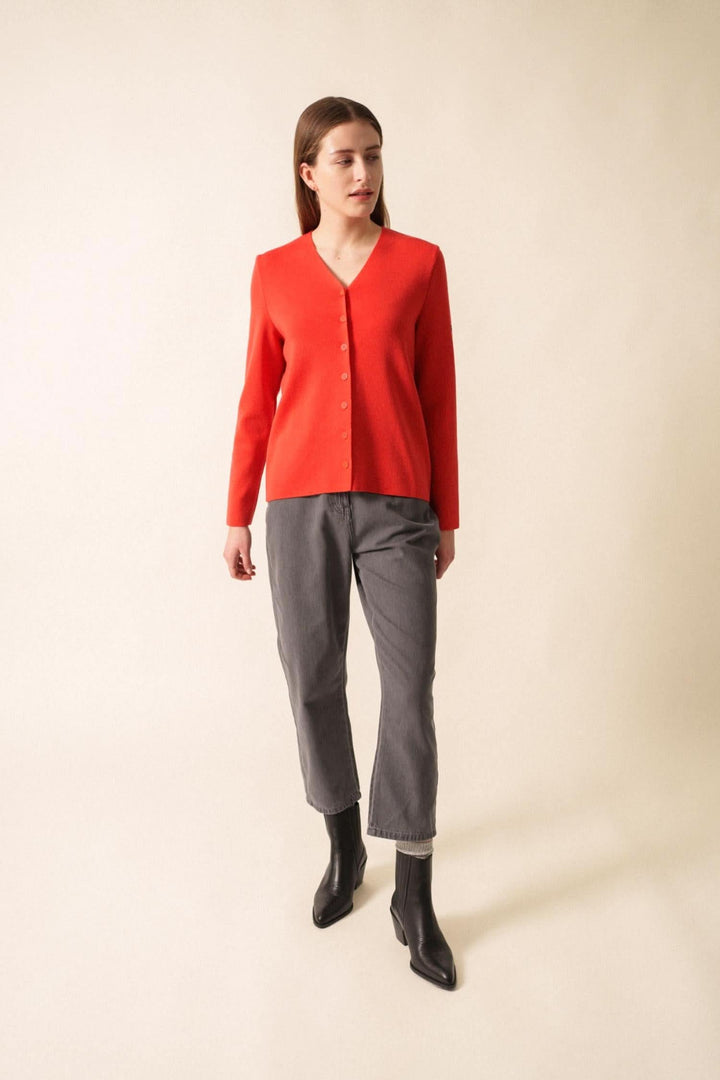 Gilet en laine rouge à encolure en V, porté avec un pantalon gris pour un look chic et minimaliste.